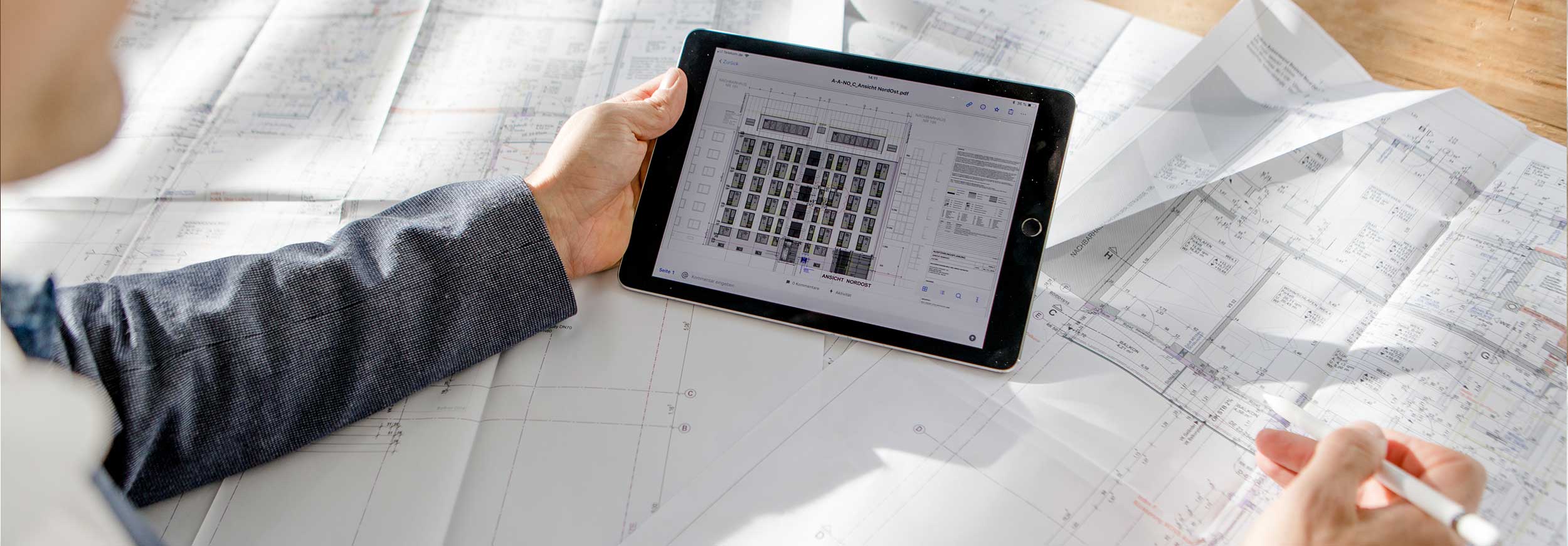 Case Köhler Bau- und Projektmanagement Architekt sitzt mit Tablet über Gebäudeplänen