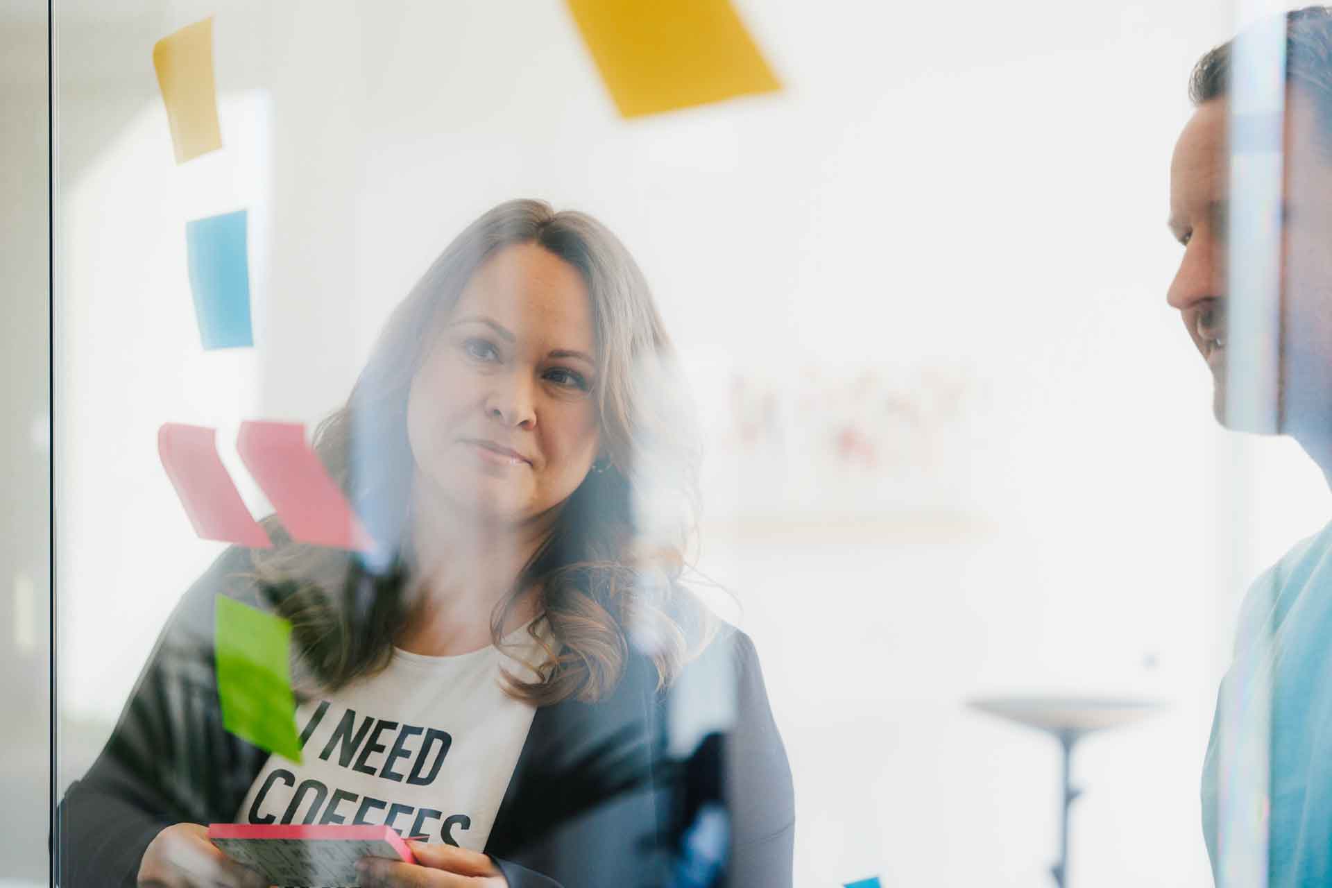 Susanne und Phil kleben bunte Post-its an die Scheibe im Meetingraum.